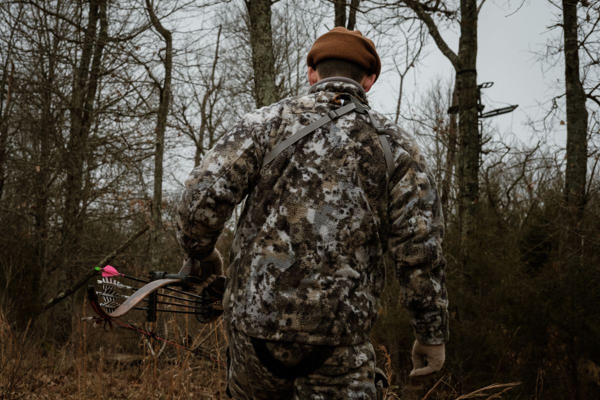 A bowhunter walking through the woods in camouflage