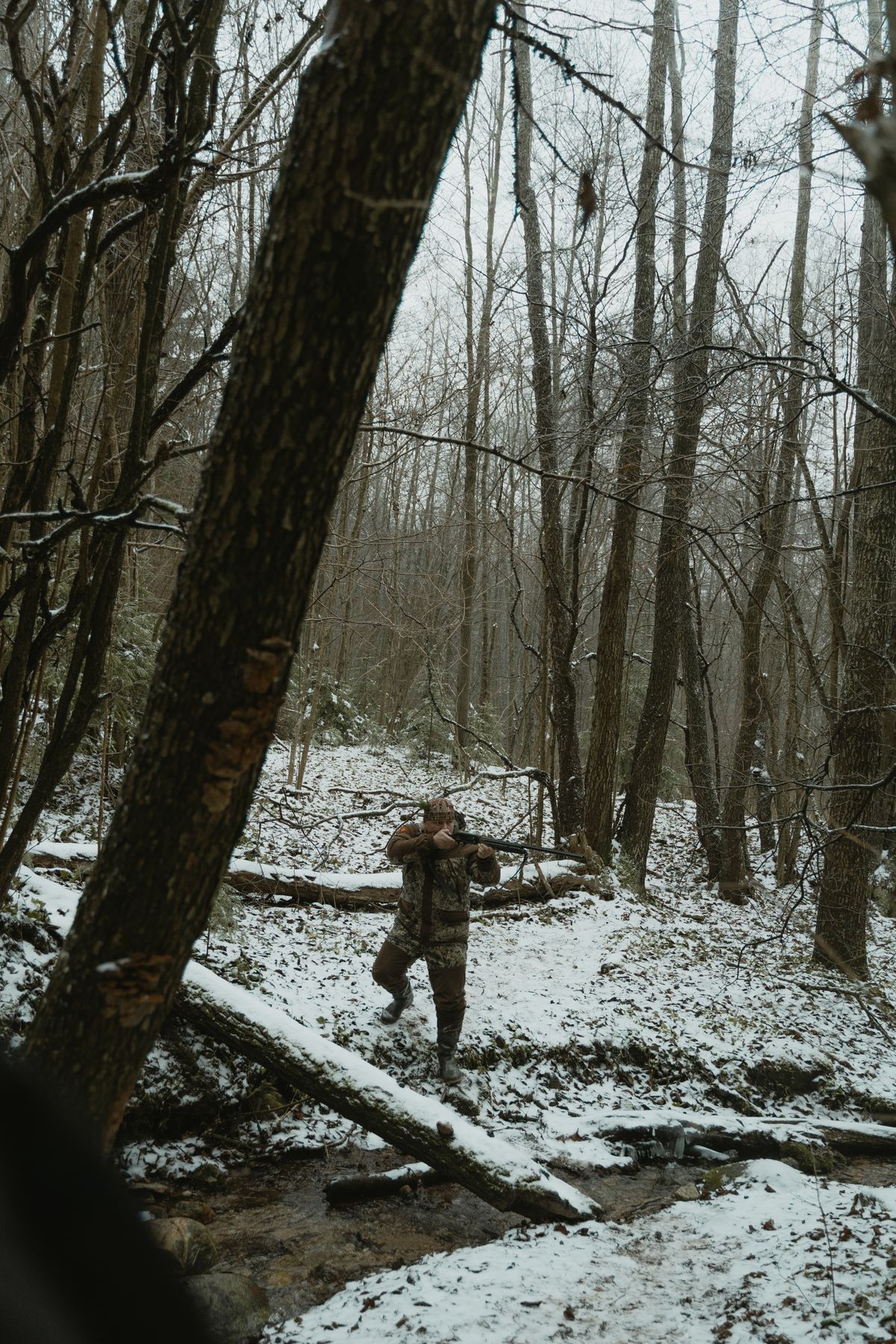 A hunter moving through a snowy woodland with a rifle